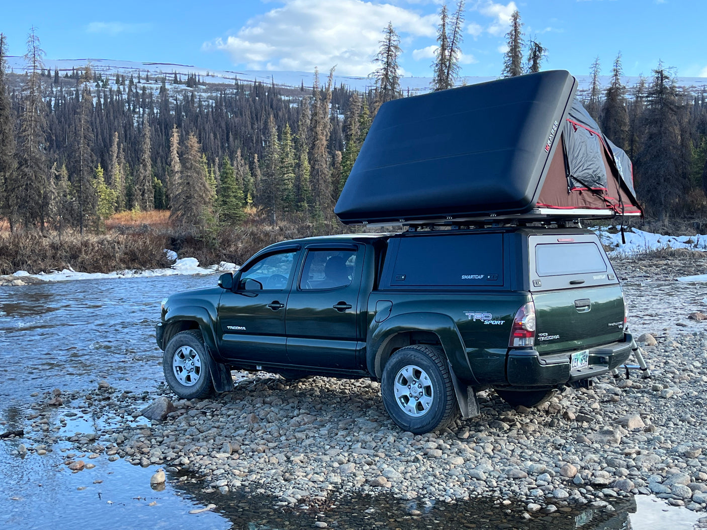 Green Toyota Tacoma truck with a rooftop tent, parked by a river. Great RV rental for off-grid adventure.