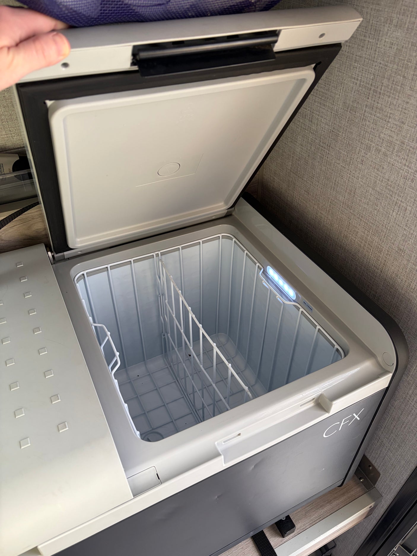 Open, empty Dometic CFX portable cooler in an RV rental, showing its wire basket and bright LED interior light.