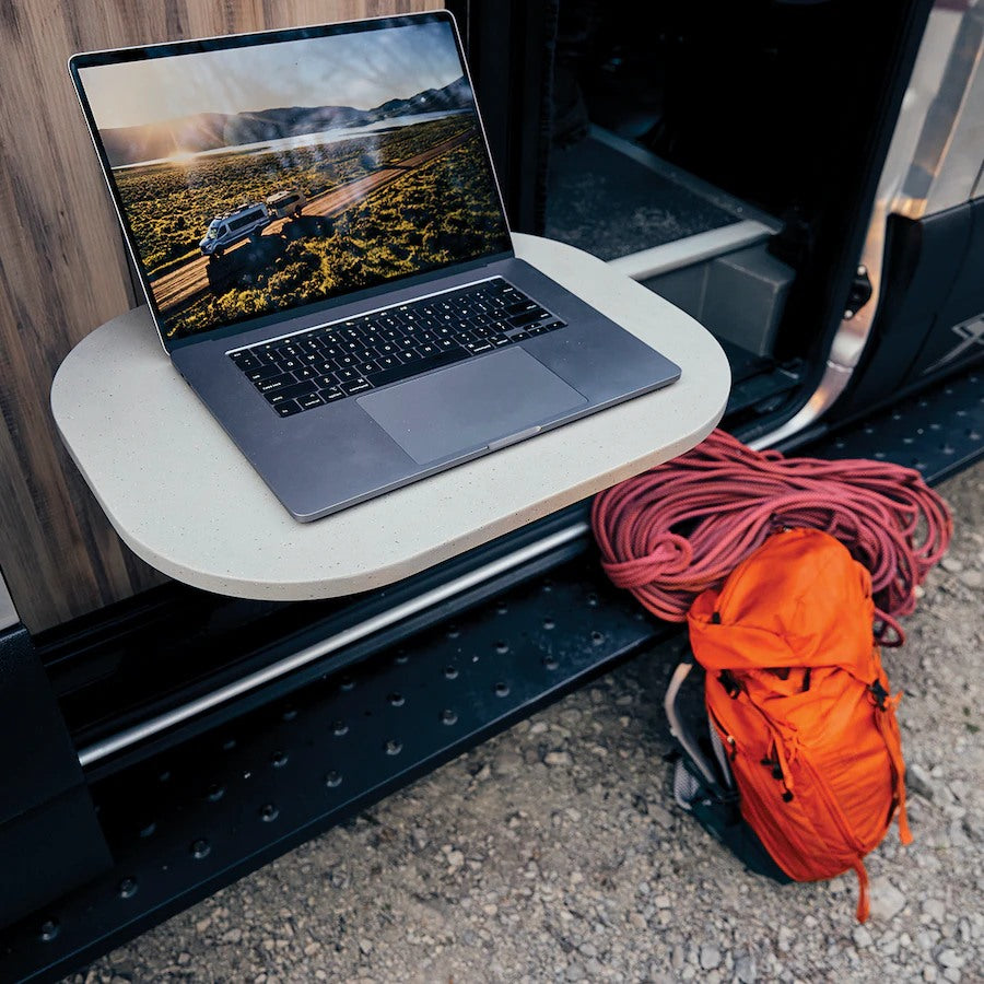 RV rental: Laptop on table shows van on scenic road. Red rope & backpack hint at adventure. Your mobile office awaits.
