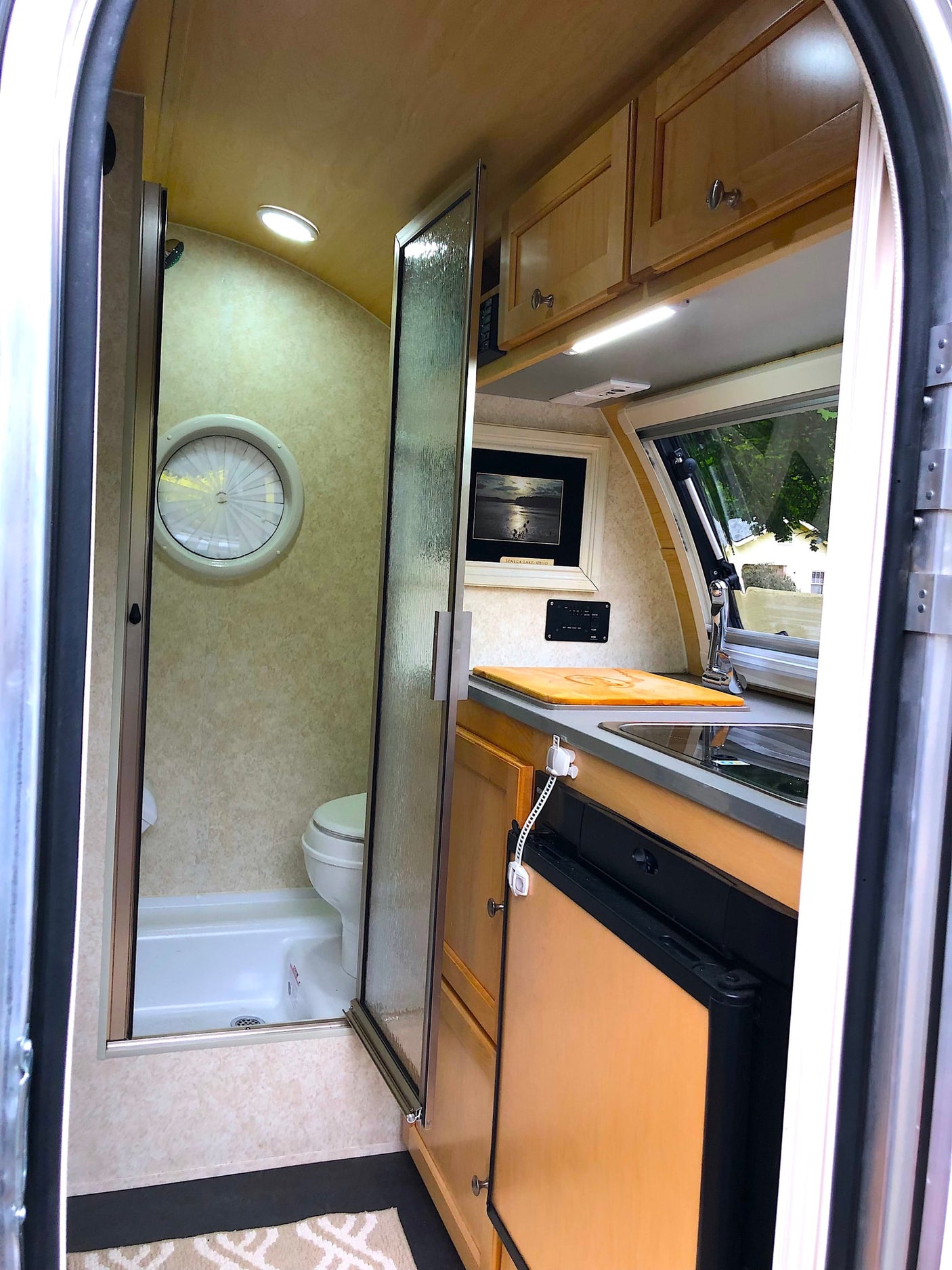 RV rental: Bright, compact camper interior featuring a kitchenette, wet bath with shower/toilet, & overhead storage.