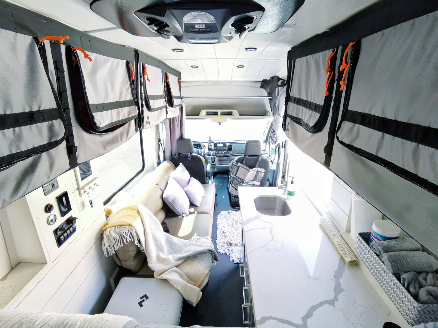 Discover this rv rental's interior: a clean kitchen, cozy lounge with pillows, and smart overhead storage in a camper van.