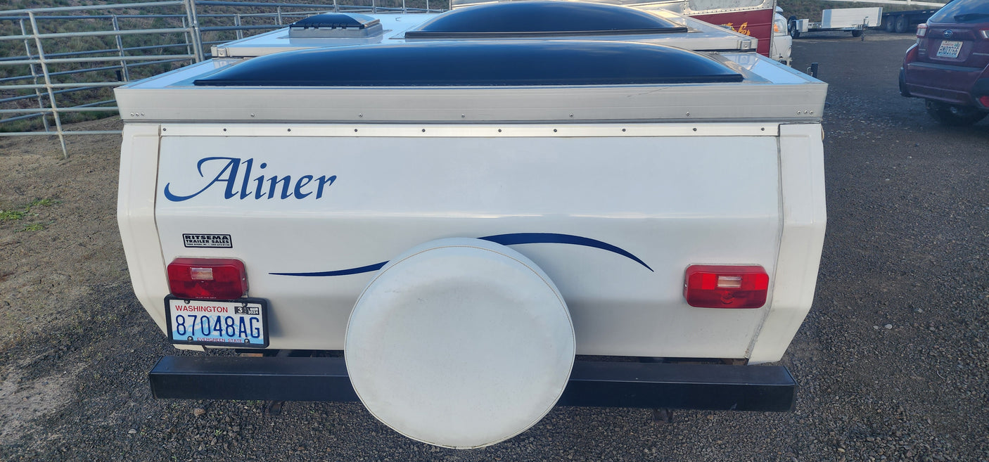 Rear view of a white Aliner pop-up camper for rv rental, displaying a Washington license plate and a rear-mounted spare tire.