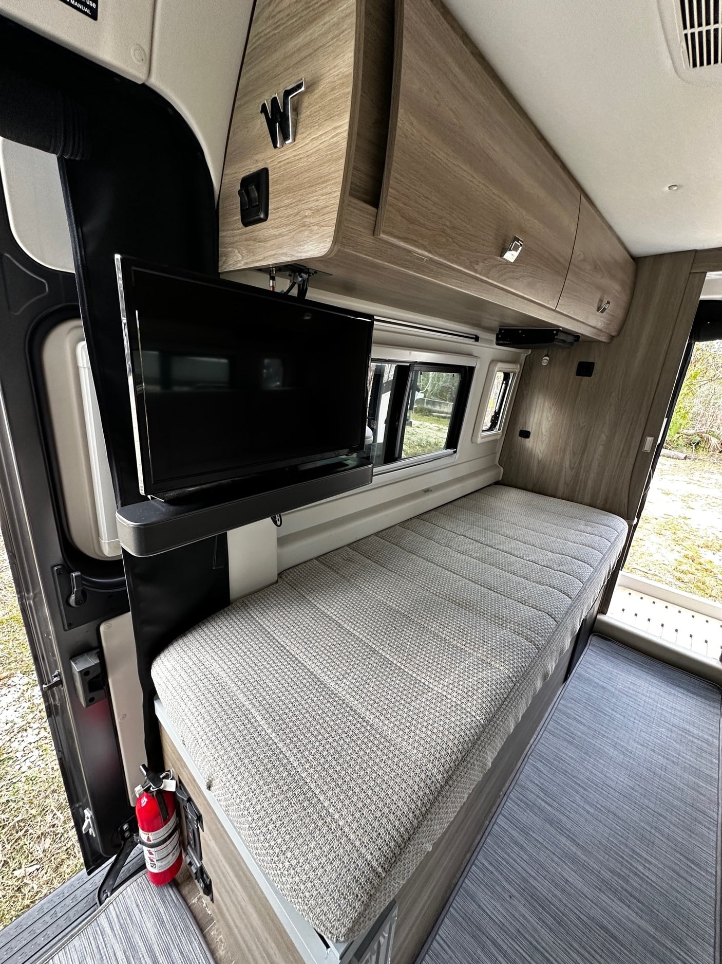 Inside this spacious RV rental, a comfy bed, wall-mounted TV, and fire extinguisher provide mobile living comfort.