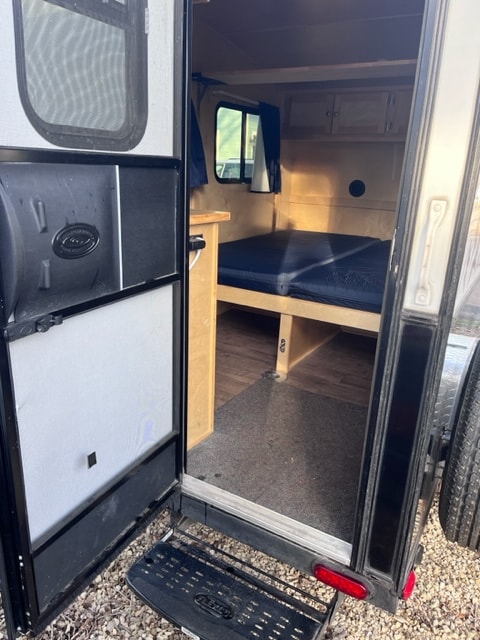 Compact rv rental interior: view through the open rear door showing a bed, cabinet, and window. Ideal for mobile adventures.
