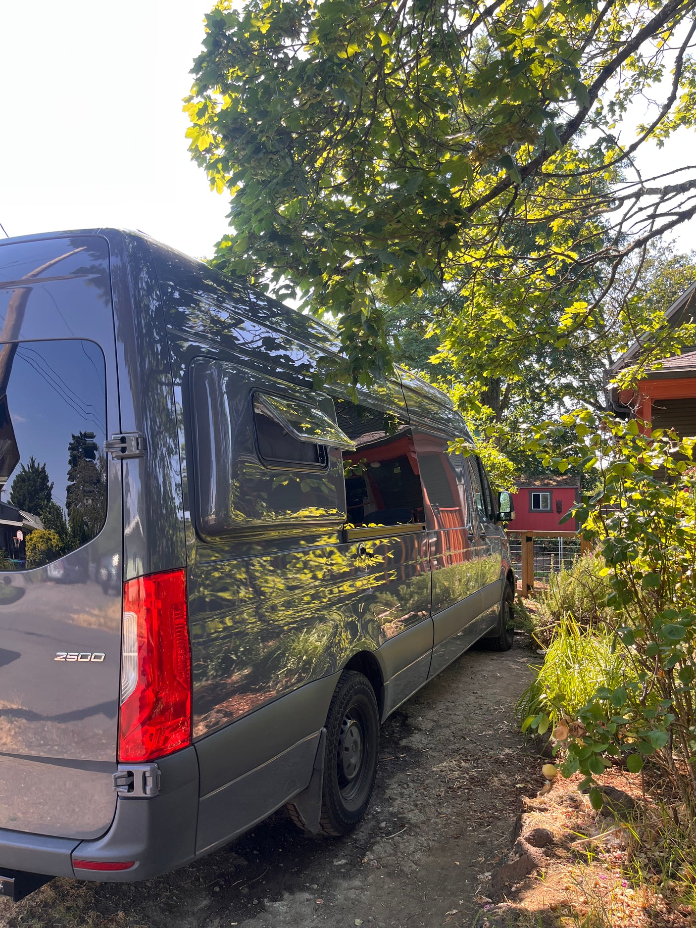 Dark grey RV rental van, a spacious Mercedes-Benz Sprinter 2500, parked outdoors under trees.