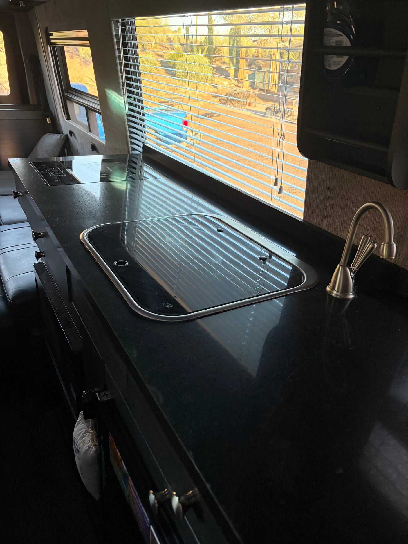 RV rental: Sleek black kitchen counter with a sink, stovetop, and desert view through window blinds.