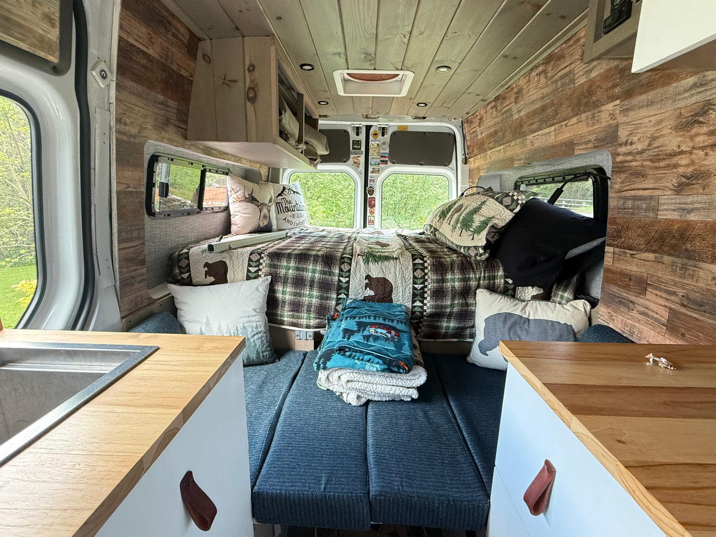 Cozy rv rental interior: wood-paneled walls, comfortable bed, compact kitchen, ideal for a scenic getaway.
