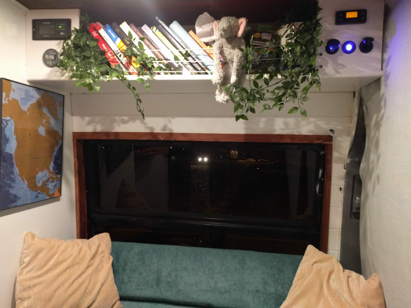 Cozy RV rental interior featuring a practical shelf with books, digital controls, map, and comfy seating.