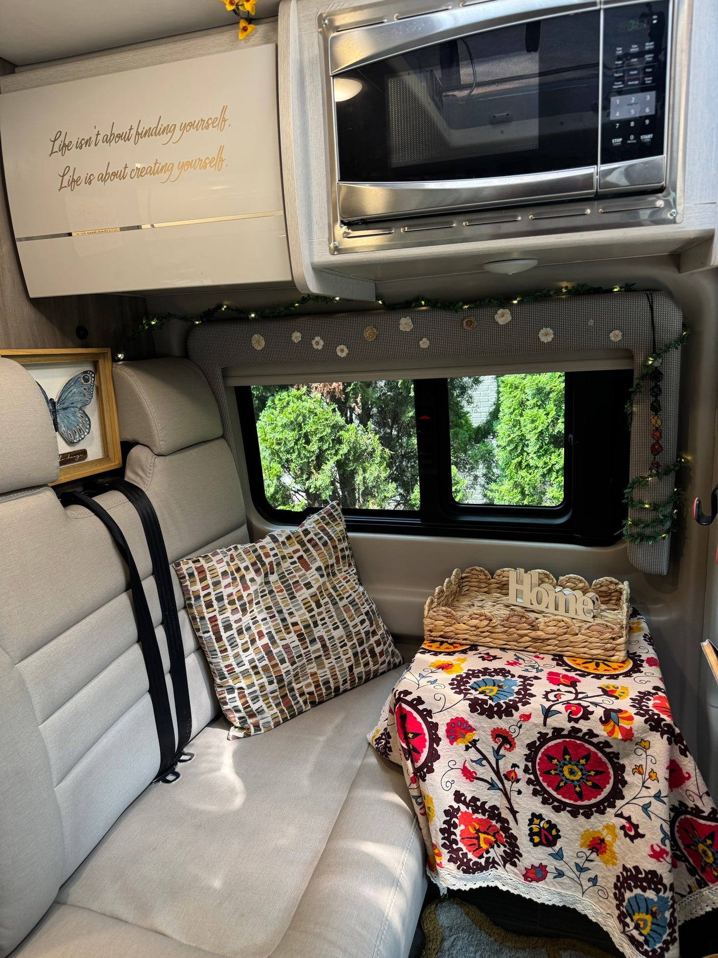 Inside a welcoming RV rental: comfy seating, microwave, colorful decor, and a window view of trees.