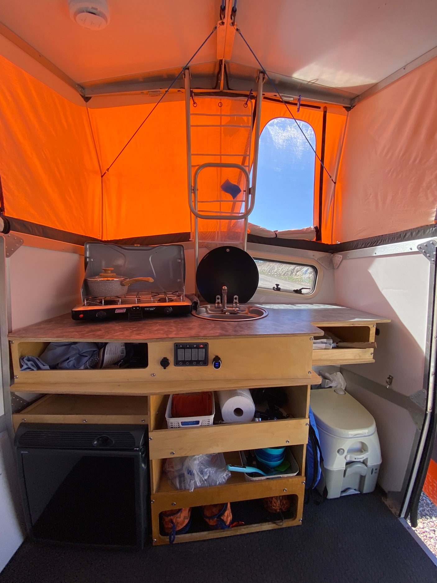This RV rental camper interior features a compact kitchen (stove, sink), ample storage, a portable toilet, and a mini-fridge.