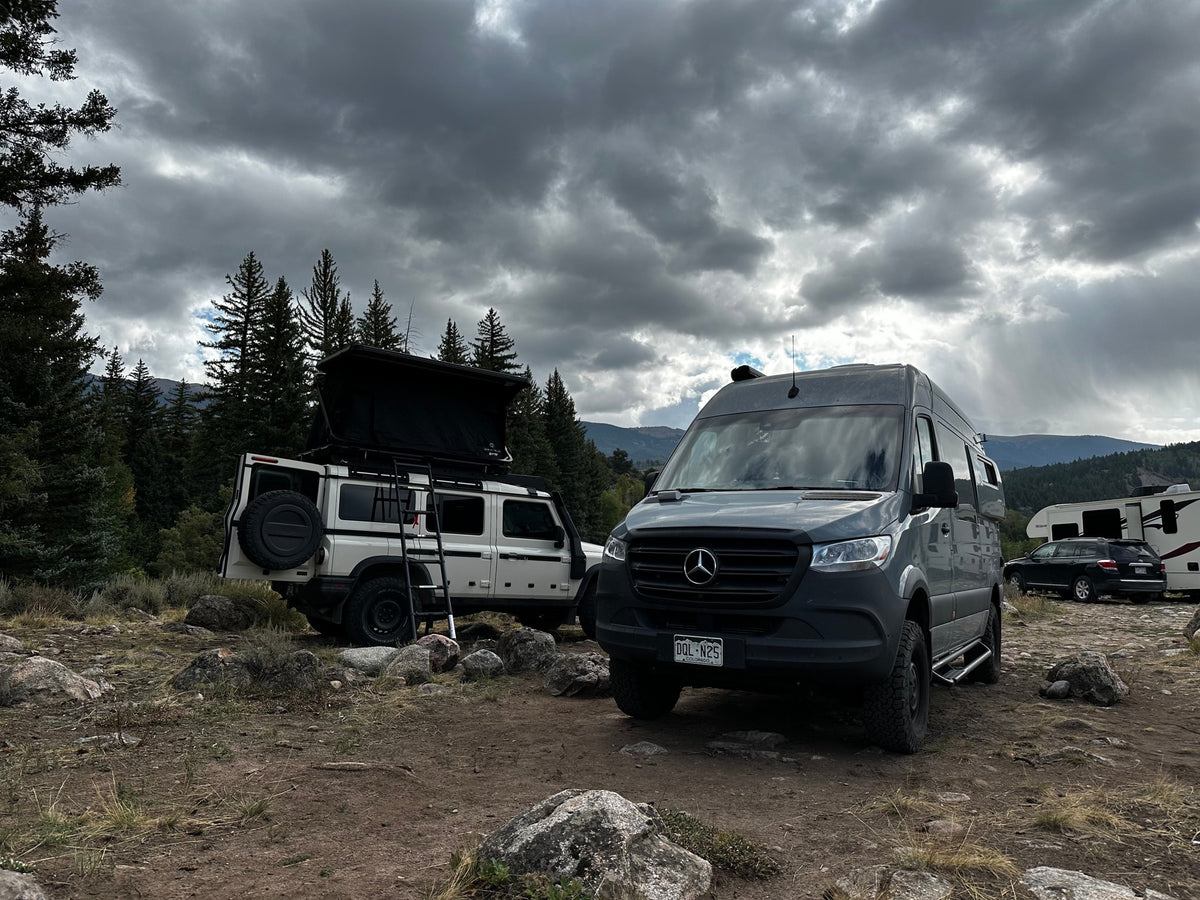 A white SUV with a rooftop tent & a grey camper van (likely an RV rental) parked at a rugged mountain campsite under cloudy skies. — photo 3