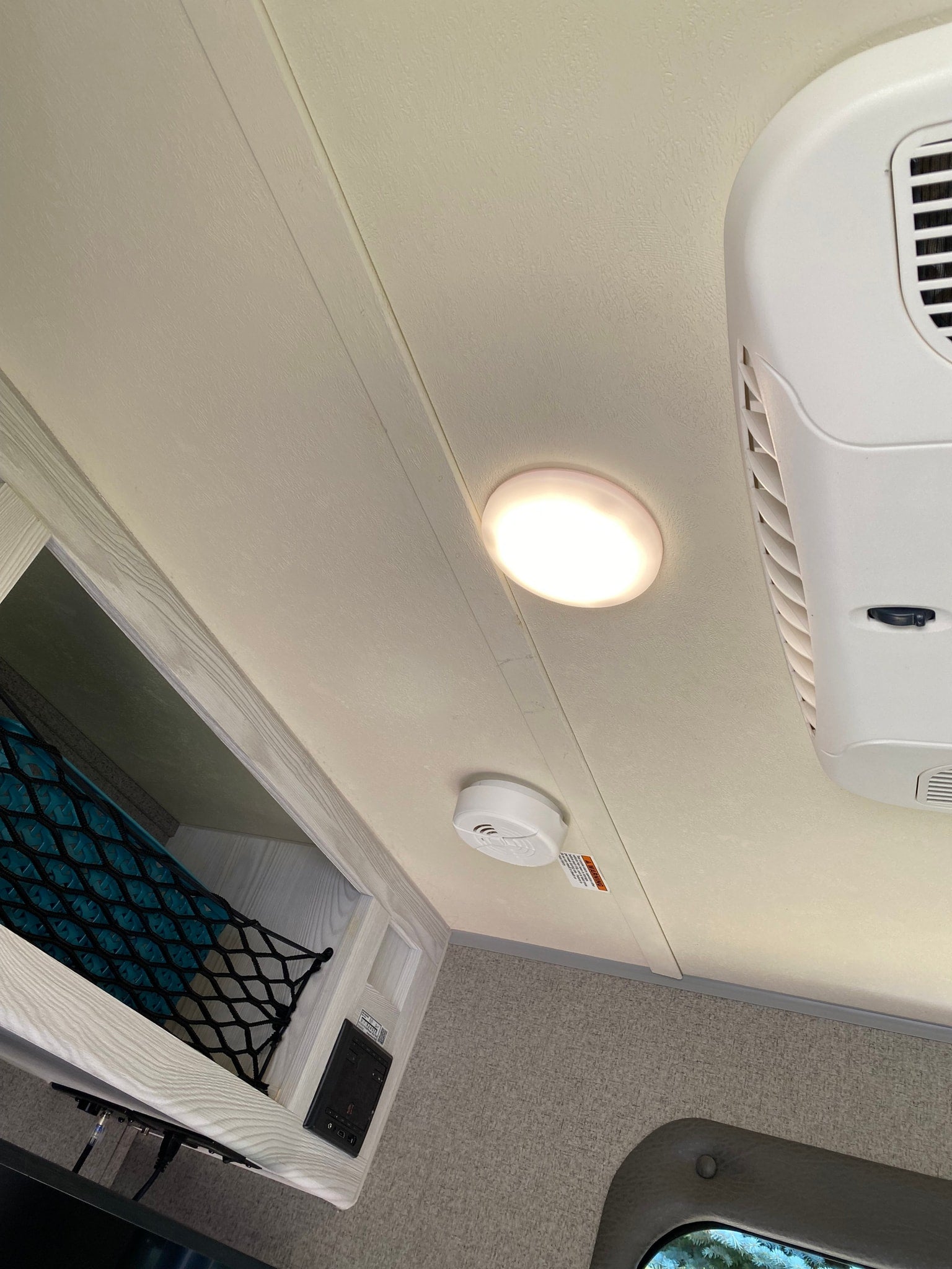 RV rental interior: Ceiling view with illuminated light, smoke detector, AC unit, and overhead storage.