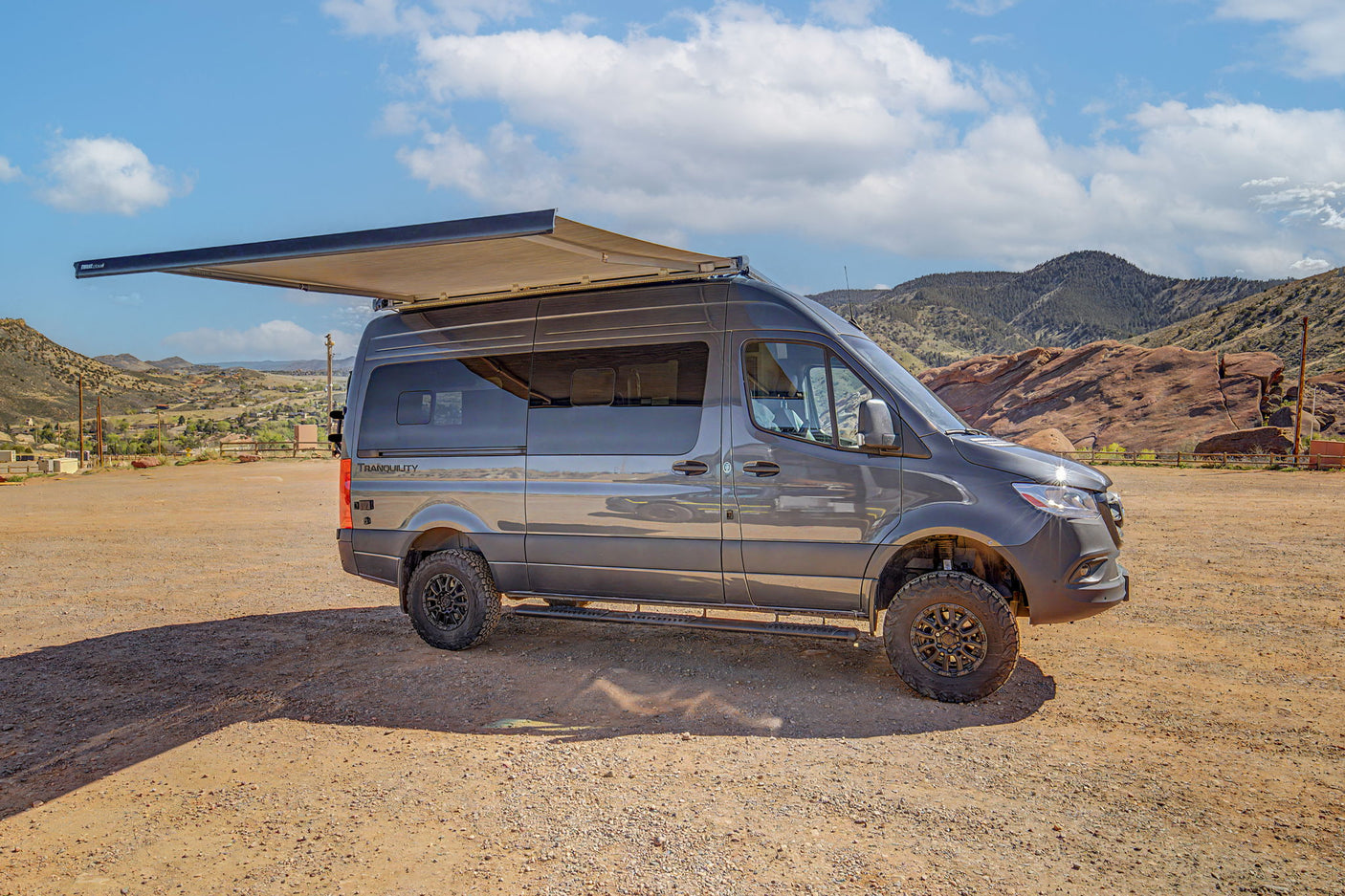 Explore the outdoors with this rv rental! A rugged gray camper van with an awning extended, parked in a scenic mountain area.