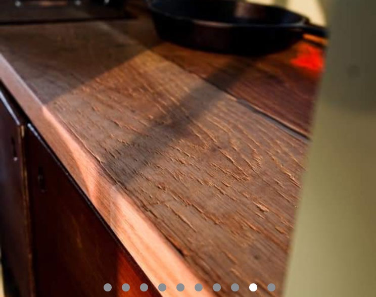 Rustic wooden countertop in an RV rental kitchen, with a cast iron pan & sunbeam. Compact living.