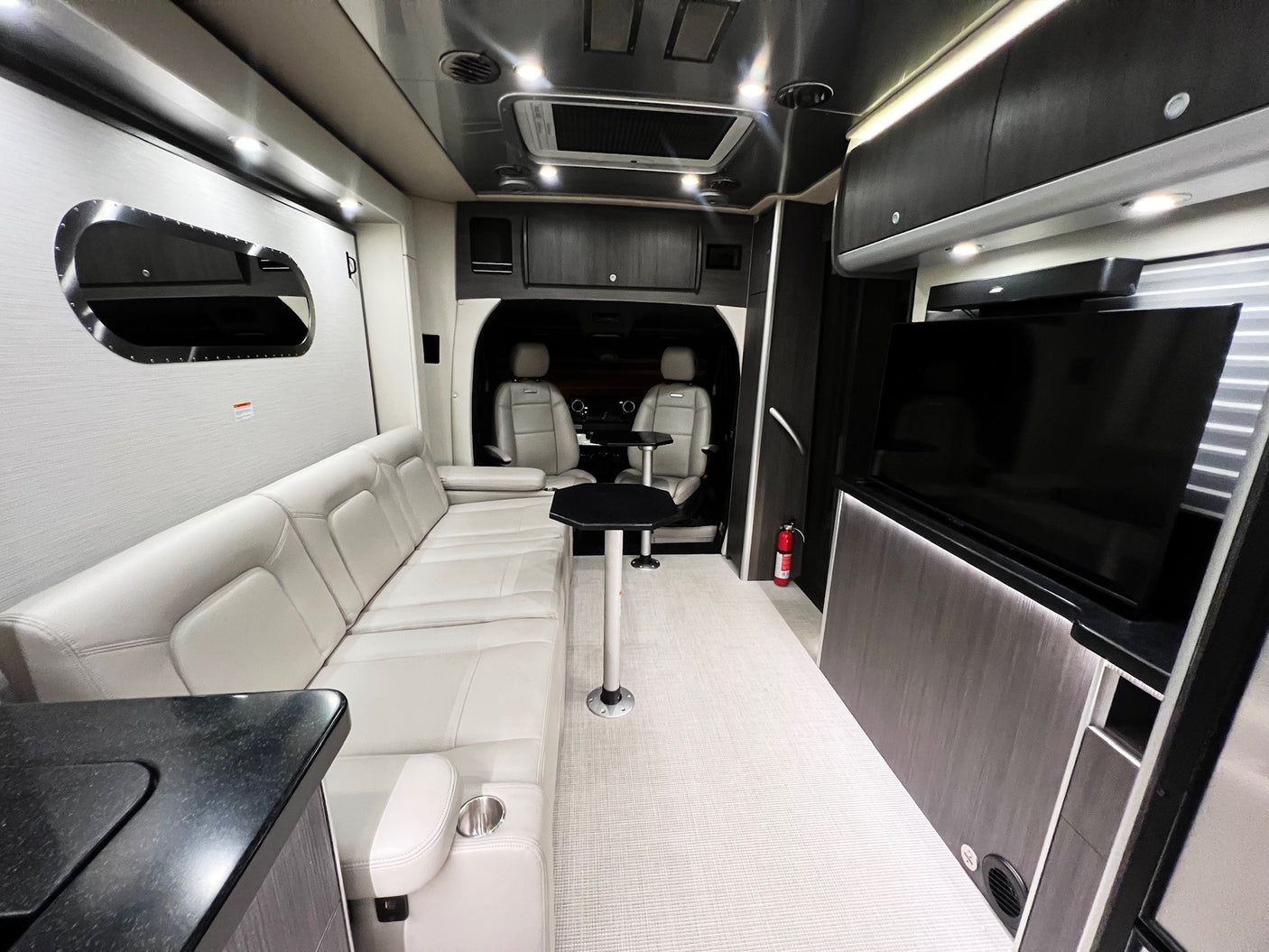 Interior of an upscale RV rental featuring a comfy sofa, dining tables, TV, & front cabin view for travel comfort.