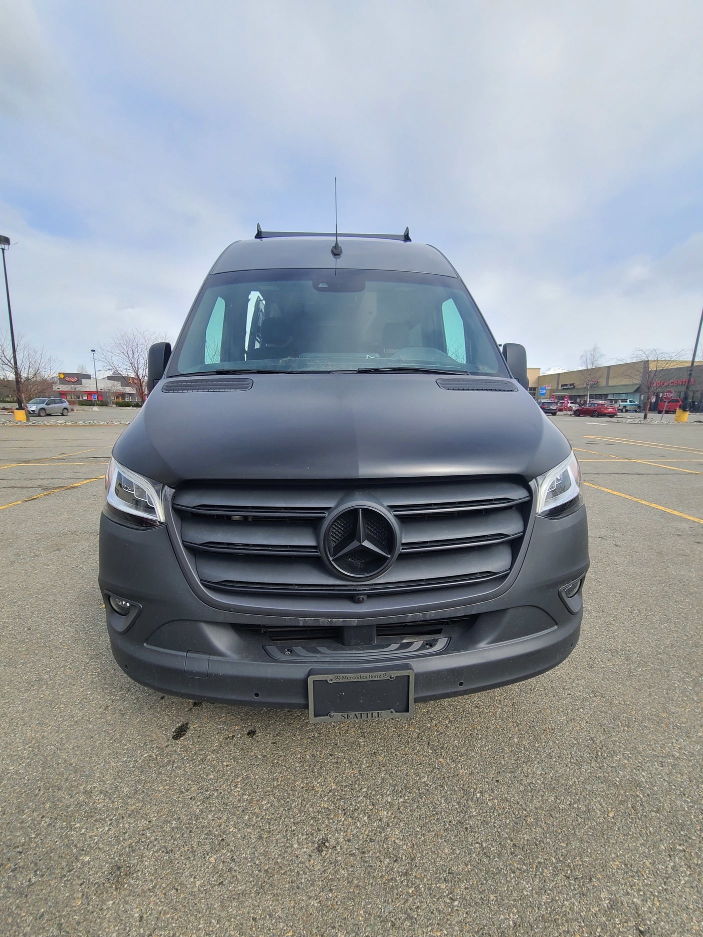 Front view of a matte black Mercedes-Benz Sprinter van, a versatile RV rental, parked in a large lot.
