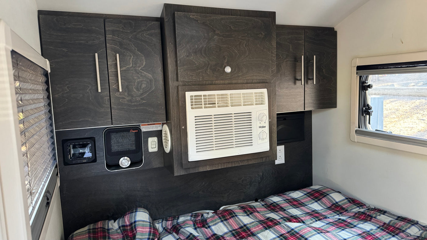 Cozy RV rental interior with bed, dark cabinetry, AC, heater, and control panel for comfort.