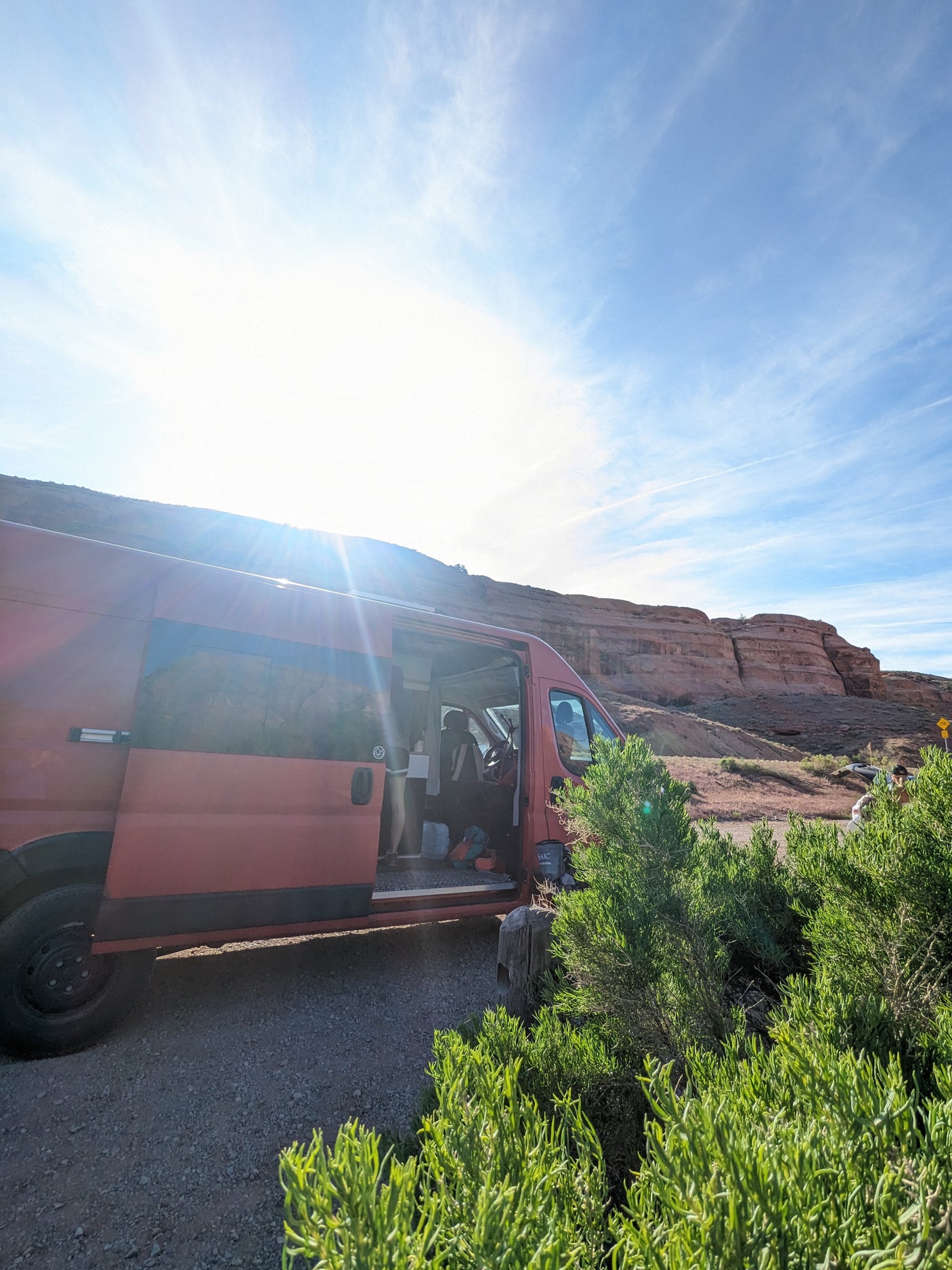 Red camper van parked with open door by red rocky cliffs on a sunny day. Your adventure starts with an RV rental!