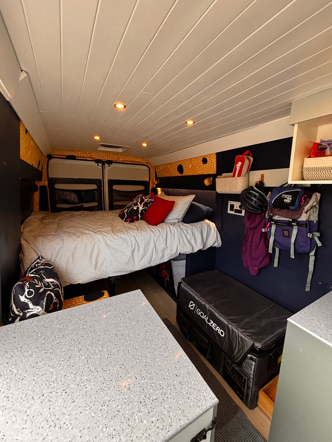 Cozy RV rental interior: A comfortable bed, ample storage including hanging gear, white slatted ceiling lights, and modern counter space.