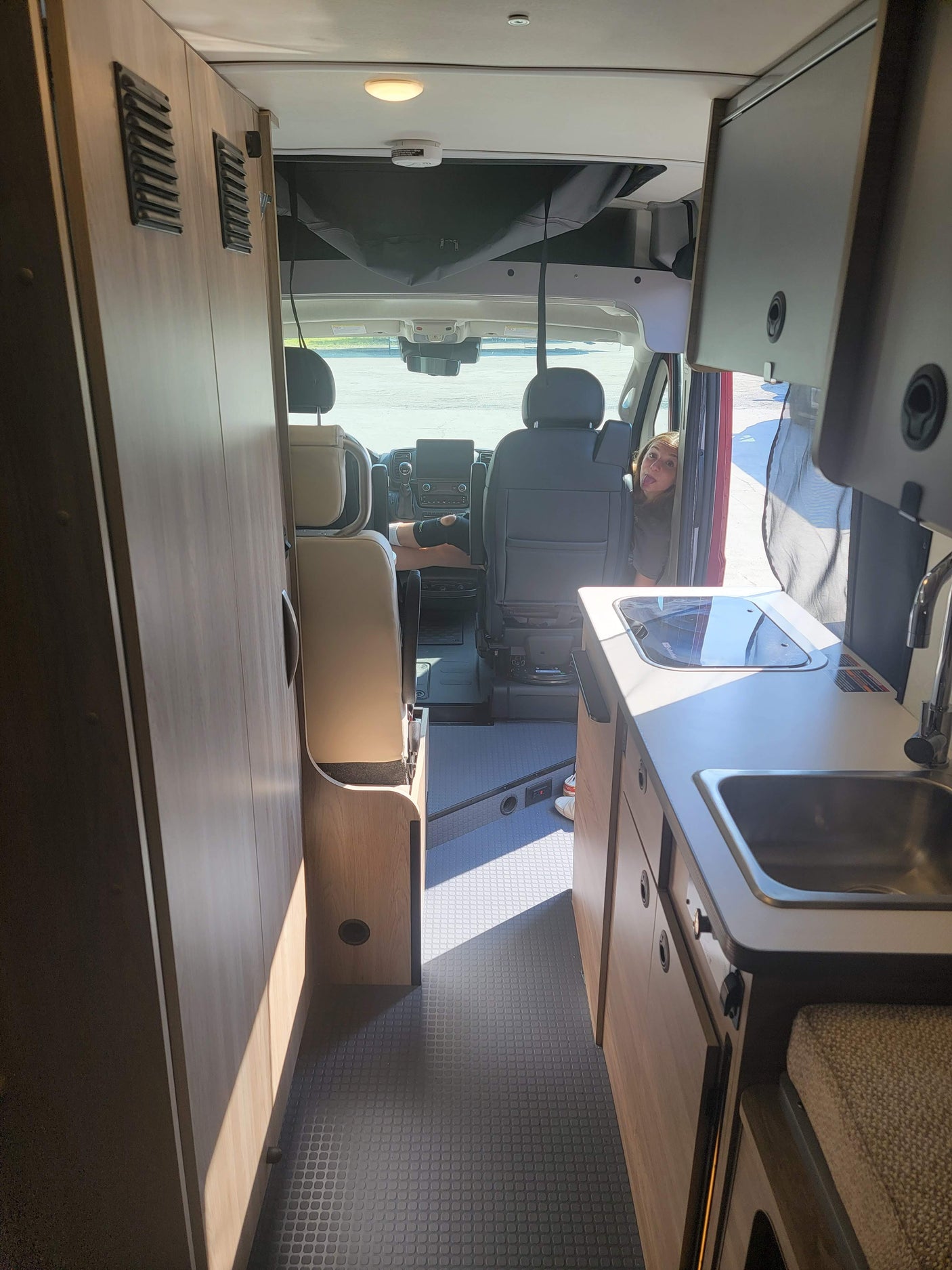 Inside a modern rv rental: kitchen, storage, and two people in the front seats, one playfully sticking out their tongue.