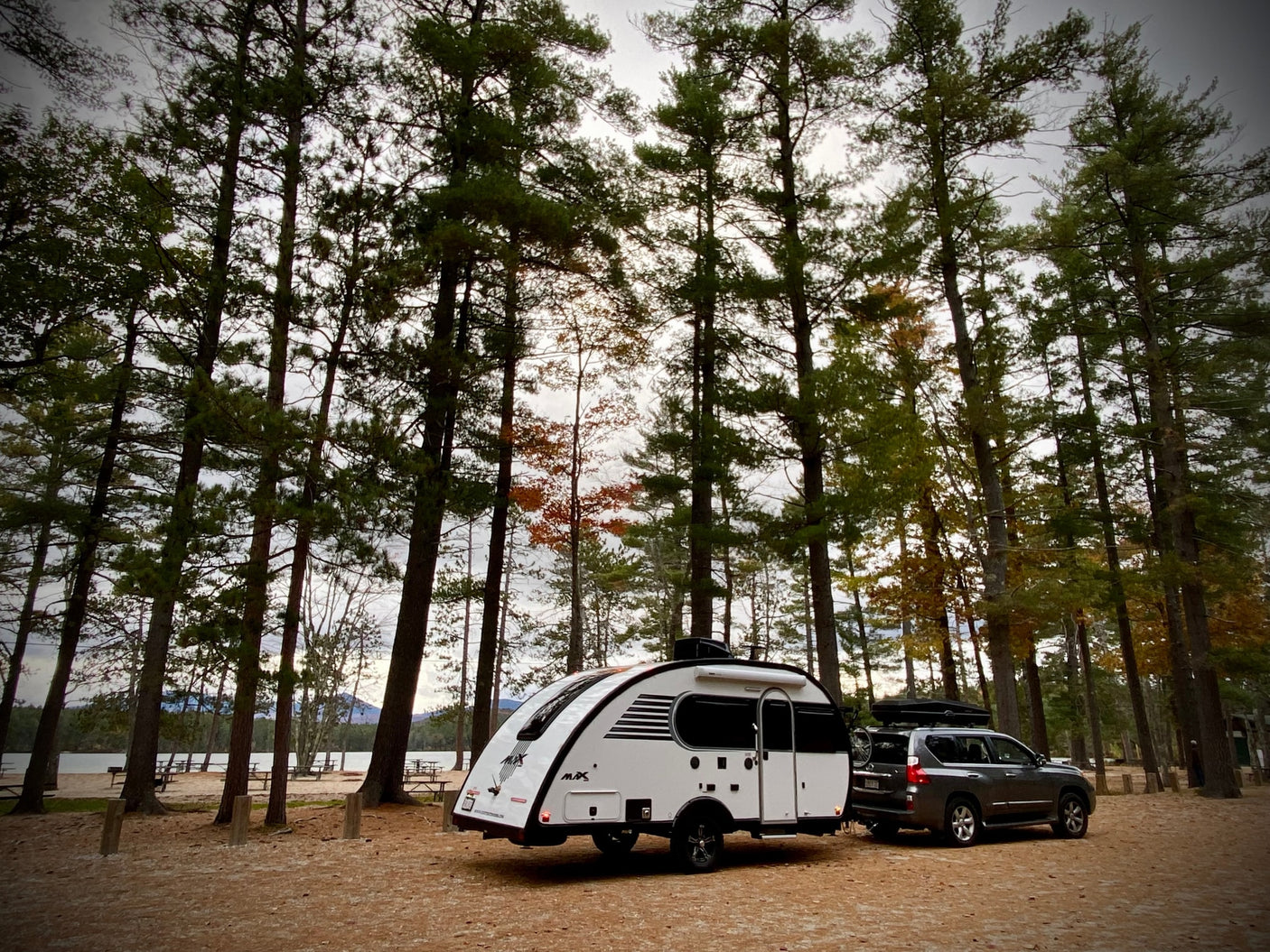 Scenic campground with an RV rental teardrop trailer and SUV by a lake. Perfect outdoor adventure!