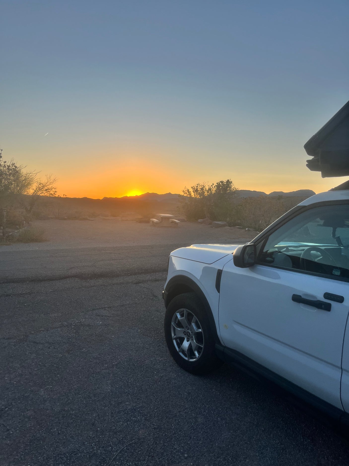White SUV with rooftop tent at desert campsite at sunset. Perfect for an RV rental road trip.