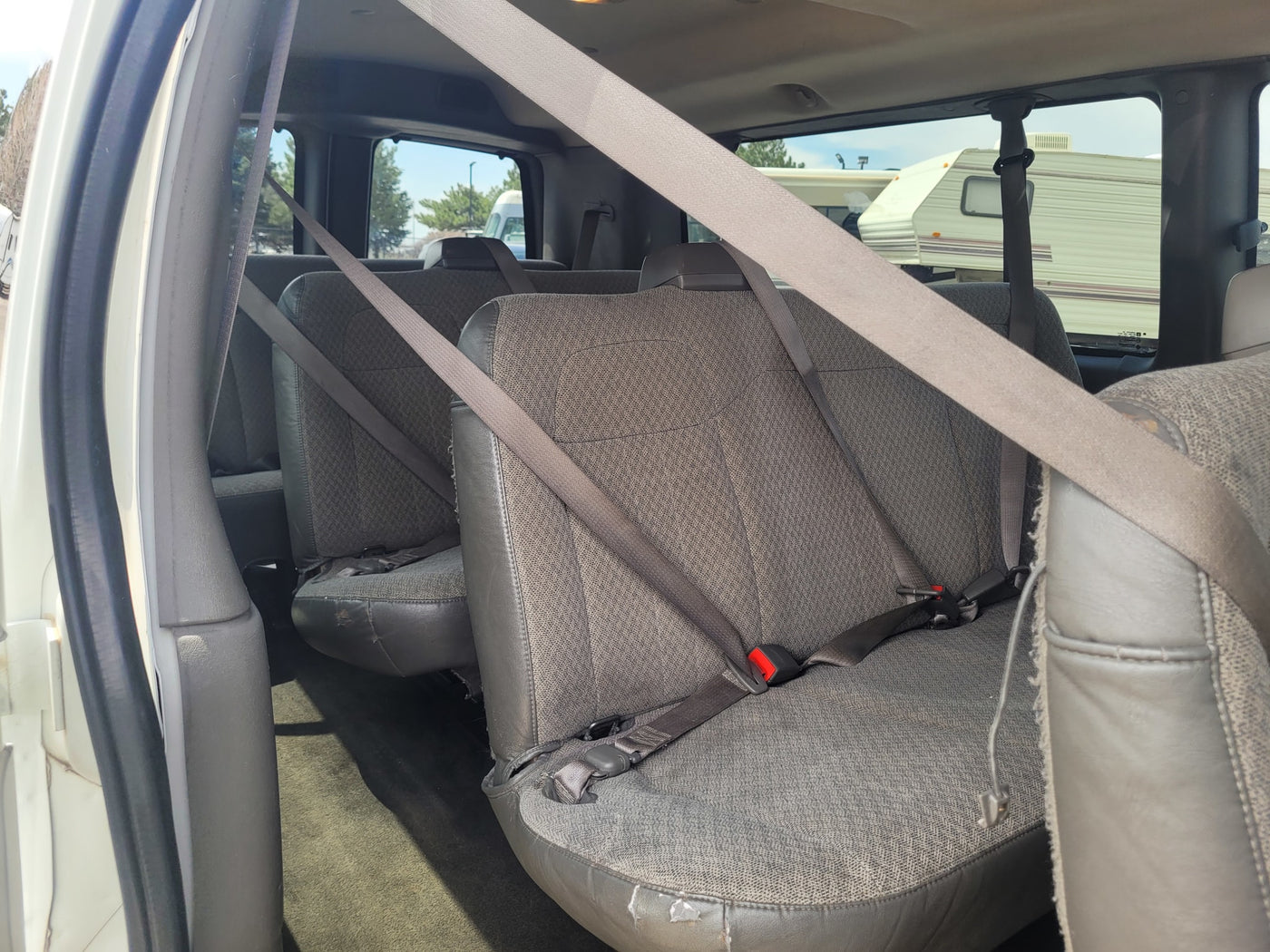 Interior of a passenger van for RV rental transport, showing rows of gray seats and seatbelts with an RV outside. — photo 6