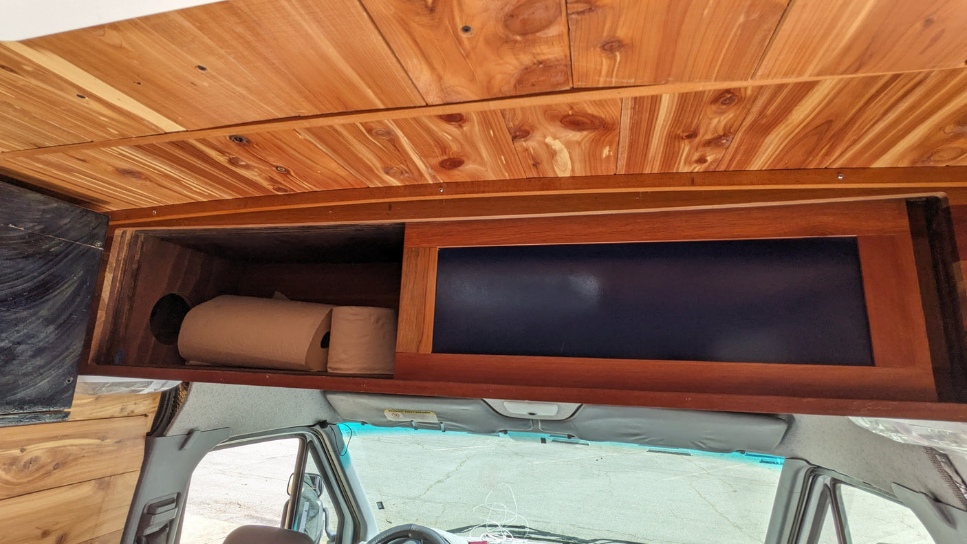 RV rental camper van overhead storage with open cabinet, paper towels, & wooden ceiling.