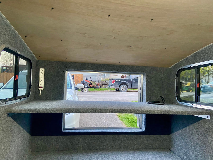 Inside an RV rental: a cozy space with carpeted walls, wooden ceiling, power strip, and scenic views from multiple windows.
