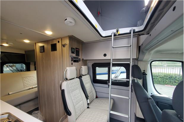 Interior of a compact RV rental, showcasing a bunk bed ladder, comfortable seating, and functional living space for travel.