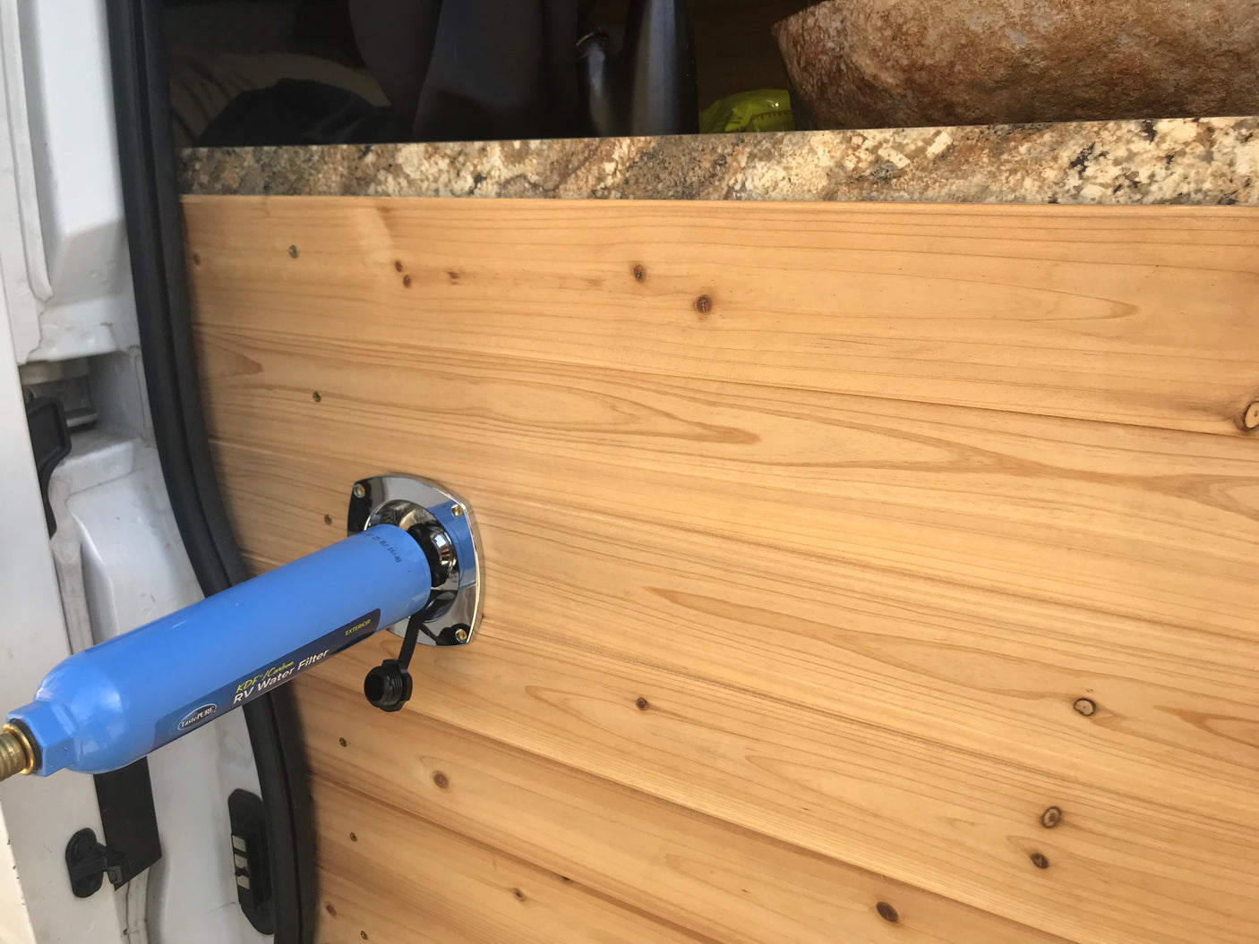RV rental ready: Blue TastePURE RV water filter mounted on the wooden interior of a camper van.