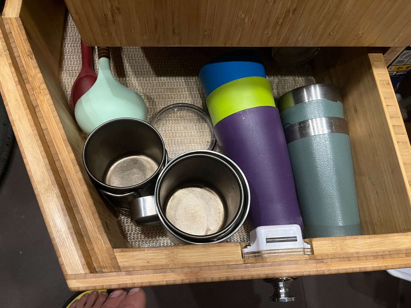 An RV rental kitchen drawer showcases neatly organized cups, tumblers, and utensils within a bamboo organizer, ideal for compact living.