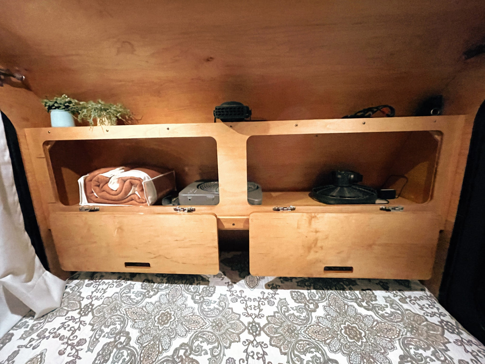 Cozy RV rental sleeping nook: patterned bed, integrated wooden shelves with blankets & fans for convenience.