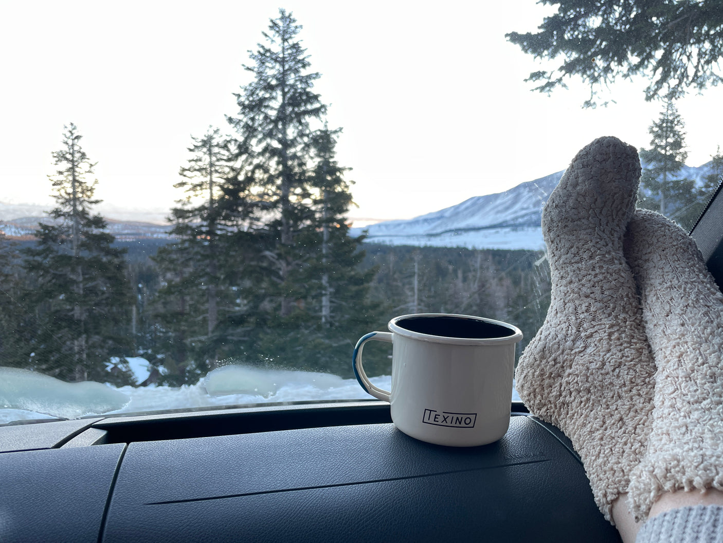 Cozy rv rental adventure: fuzzy socks, warm mug on dash, serene snowy mountains outside the window.