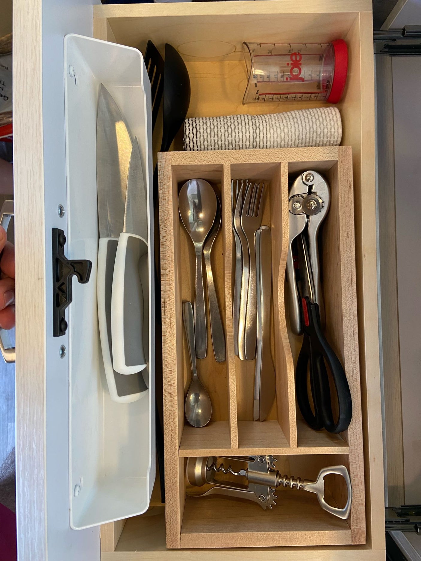 Compact kitchen drawer organization for an RV rental. Knives, cutlery, measuring cup, and tools like a can opener are neatly stored.