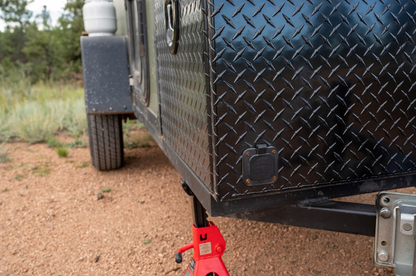 Close-up of a robust black diamond plate RV rental trailer, featuring a power inlet and red jack, for outdoor adventure.