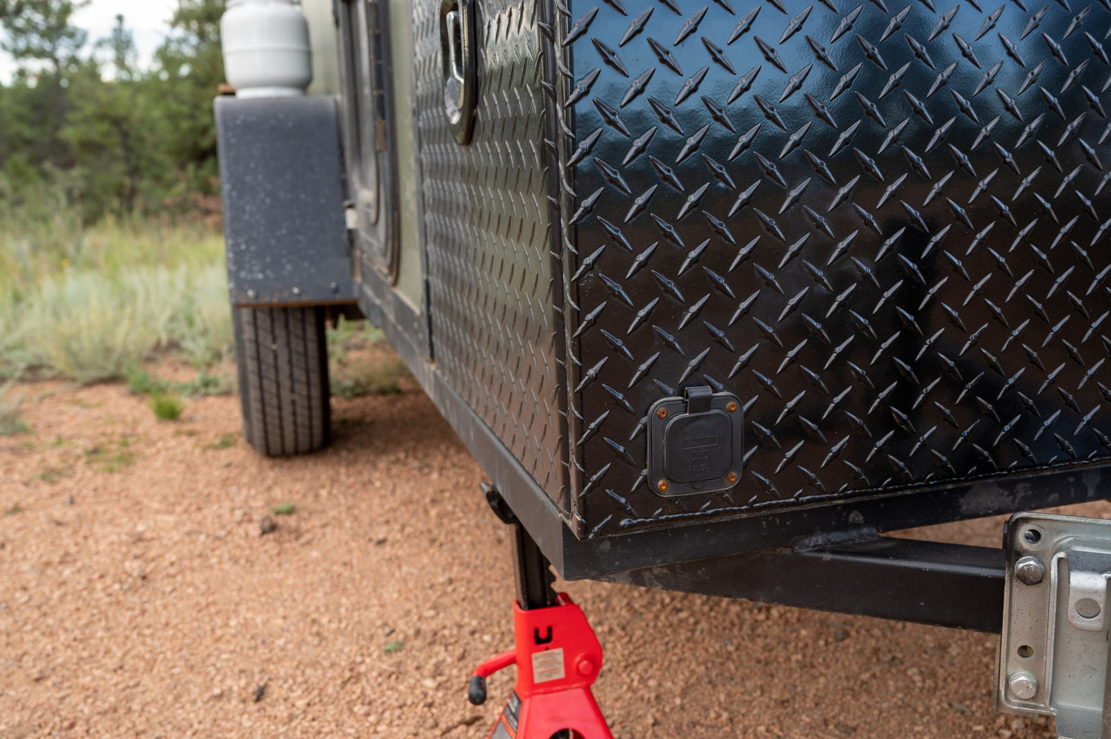 Close-up of a robust black diamond plate RV rental trailer, featuring a power inlet and red jack, for outdoor adventure.