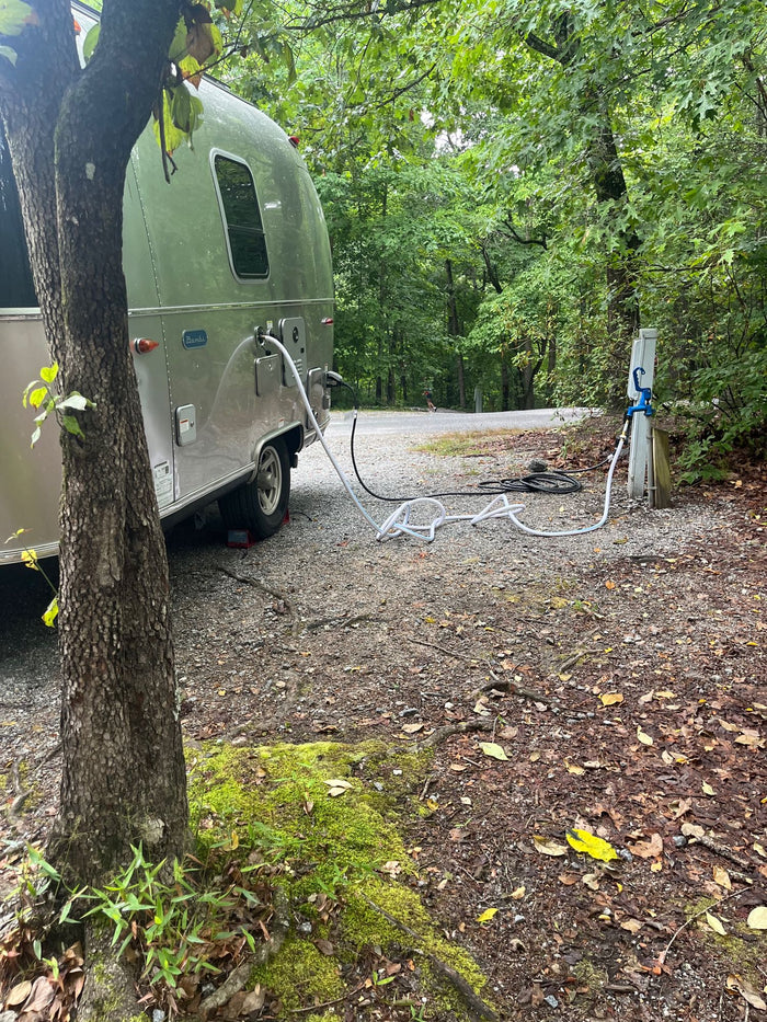 parked on a paved drive under autumn trees.|RV rental: A silver Airstream travel trailer hooked up at a tranquil