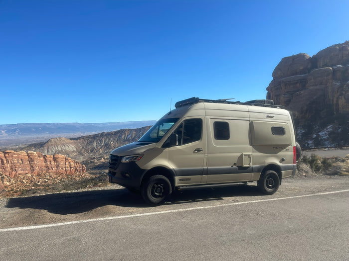 parked on a desert roadside overlooking a vast valley and distant mountains.|A beige Winnebago Revel 4x4 camper van (RV rental) on a scenic mountain road