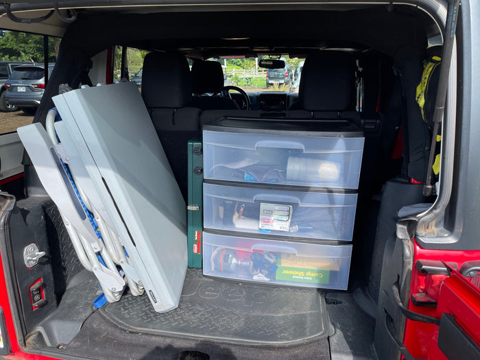 Back of a Jeep packed with camping gear for an RV rental trip: table, Coleman propane stove, and storage drawers.