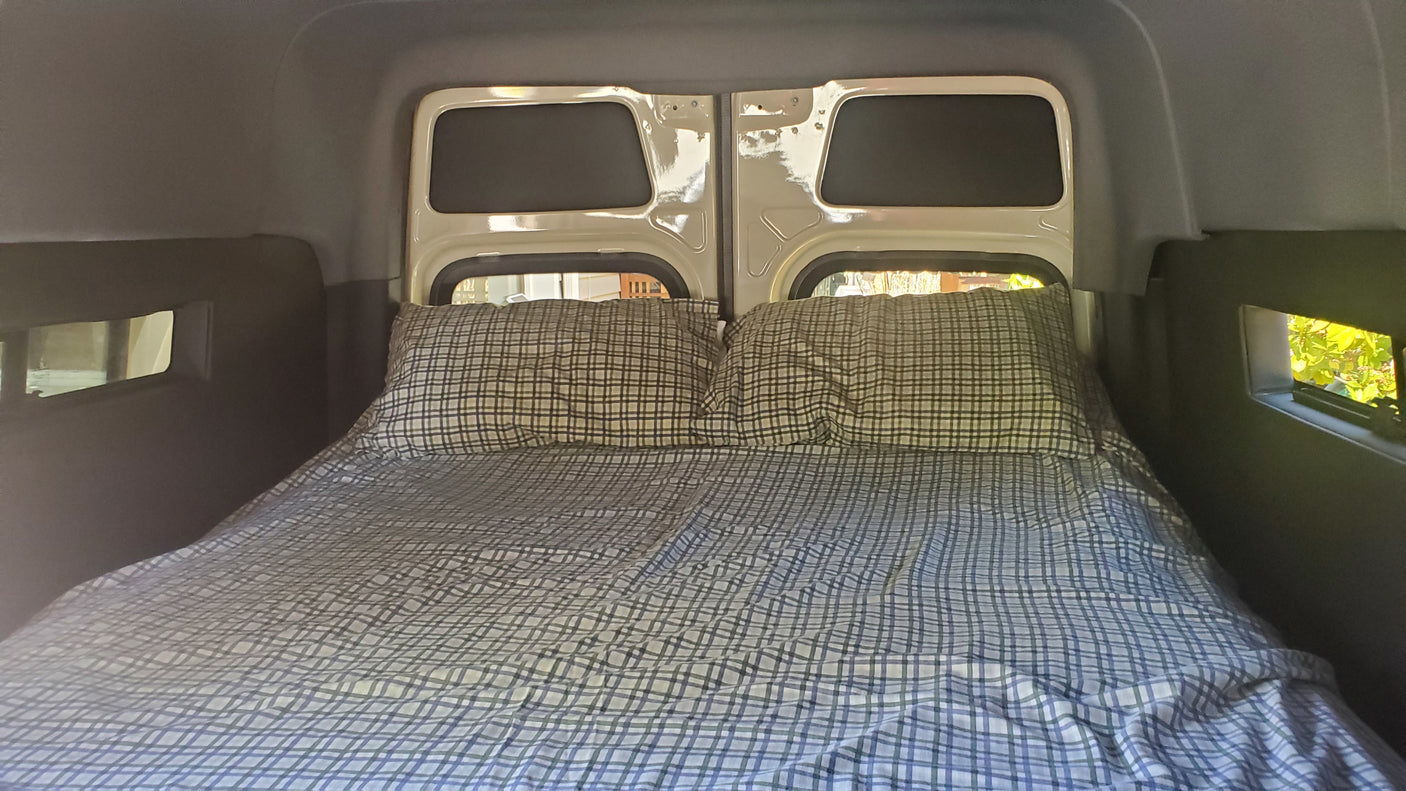 Comfortable rv rental bed with plaid sheets and rear windows, ready for a good night's sleep in your camper van.