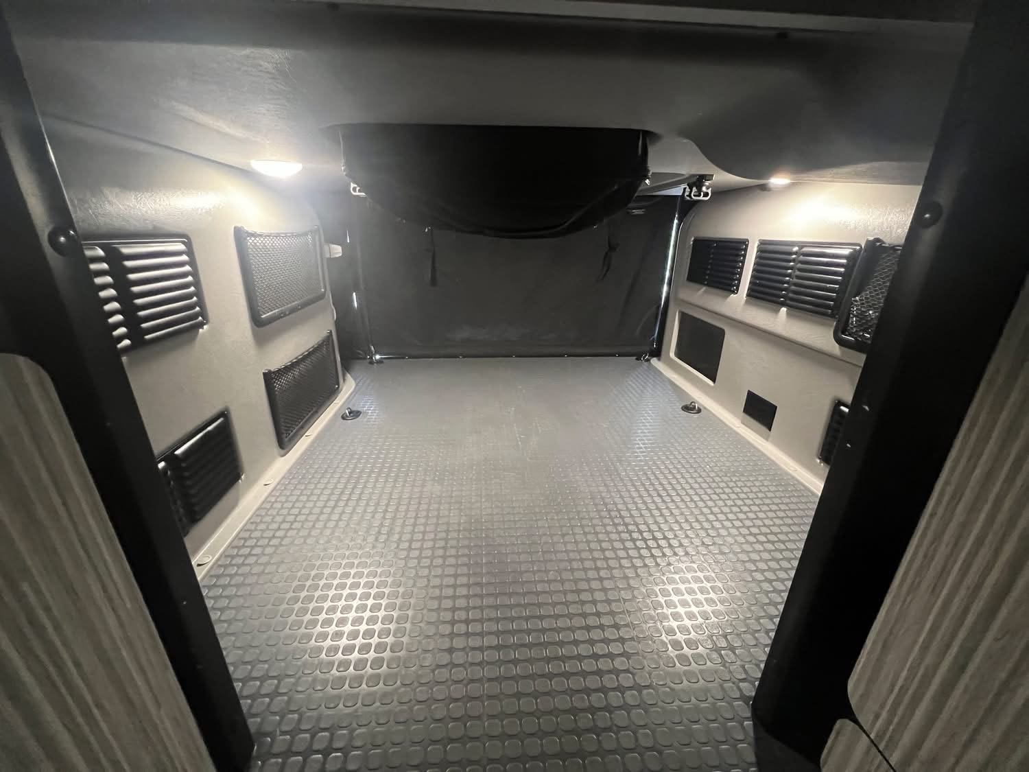Spacious, empty RV rental interior with textured floor, wall vents, and bright overhead lighting, ready for your adventure.