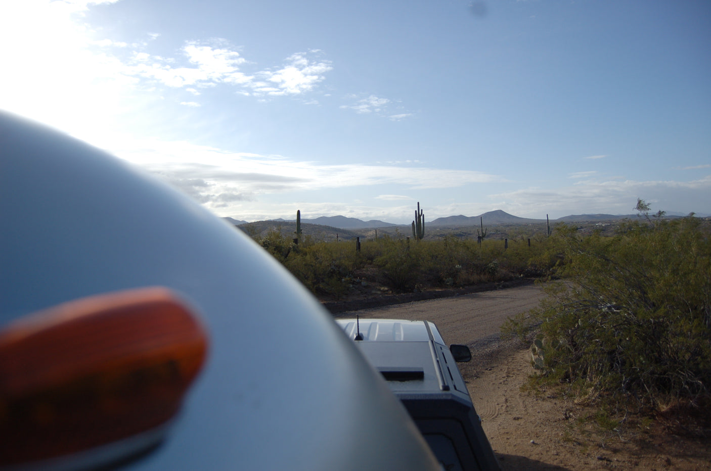 Desert adventure from an RV rental! Enjoy scenic views of saguaro cacti, mountains, and a dirt road under a bright sky.