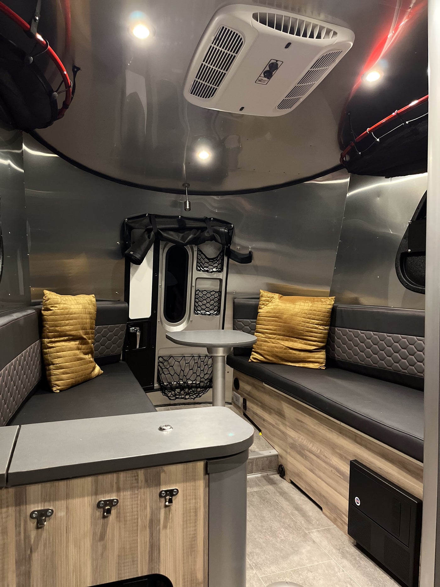 View inside a modern RV rental featuring metallic walls, black seating with yellow cushions, a table, and overhead AC. — photo 13