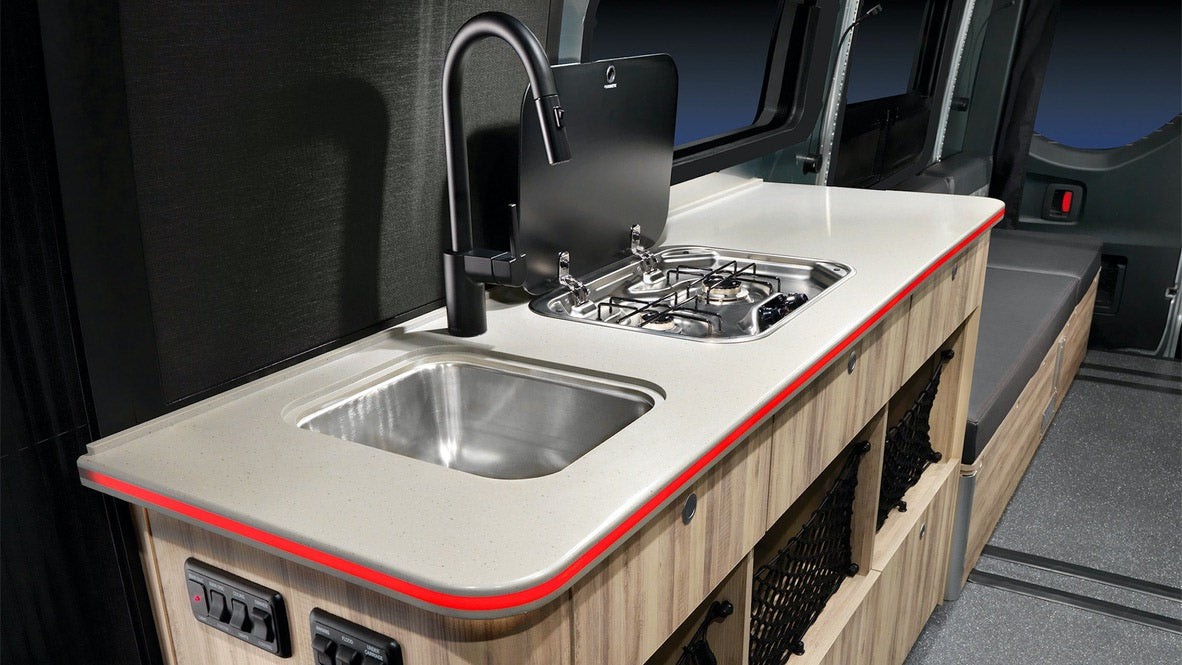 RV rental kitchen: compact design with sink, 2-burner stove, and illuminated counter. Ideal for mobile adventures.