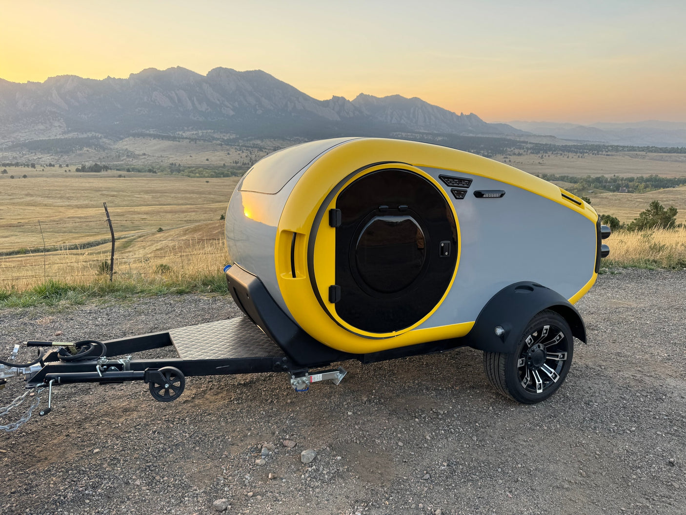 Modern yellow & gray compact travel trailer, an ideal RV rental, set against scenic mountains.
