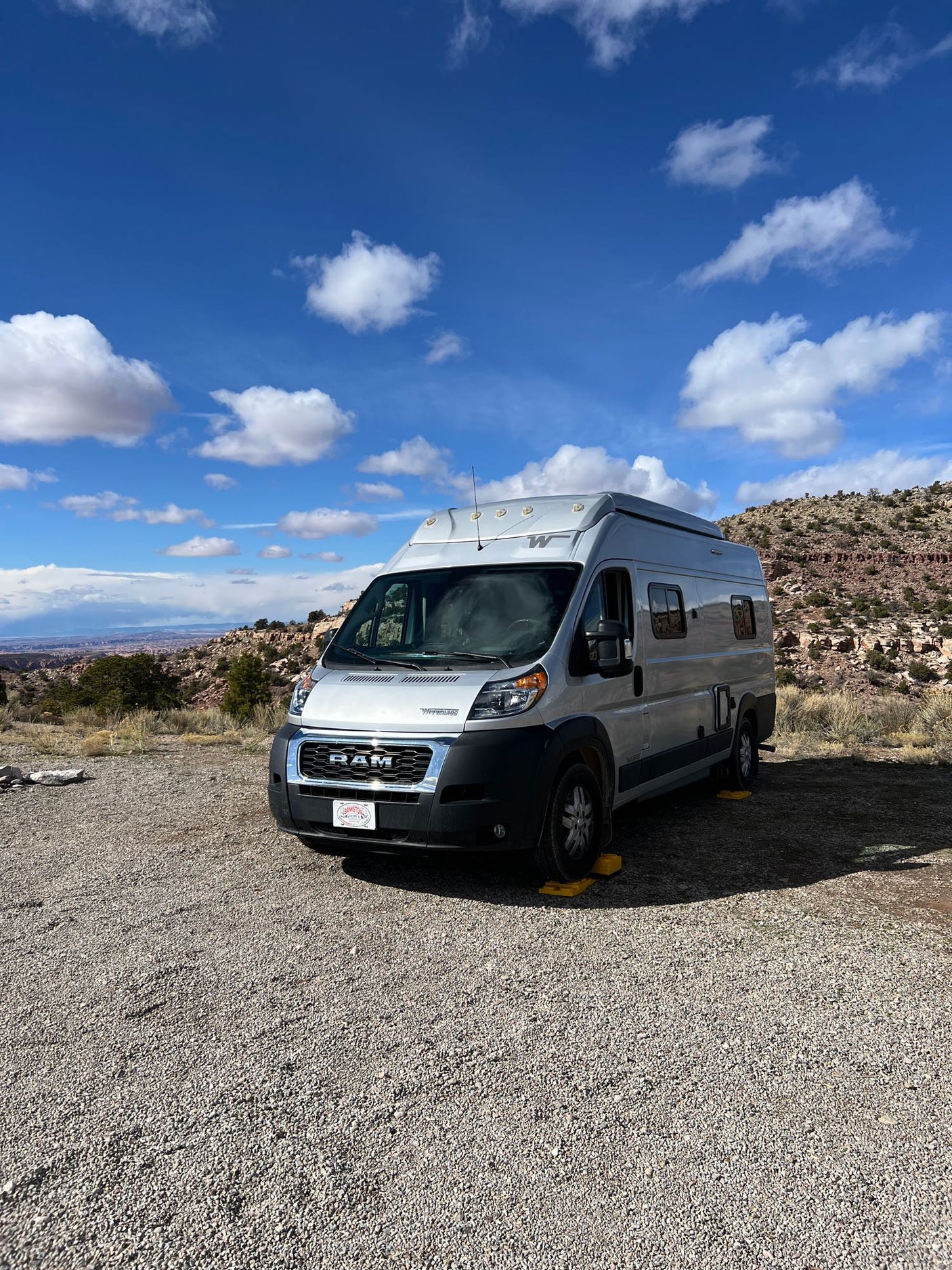 Silver Winnebago rv rental camper van leveled on gravel, with desert landscape and blue sky.