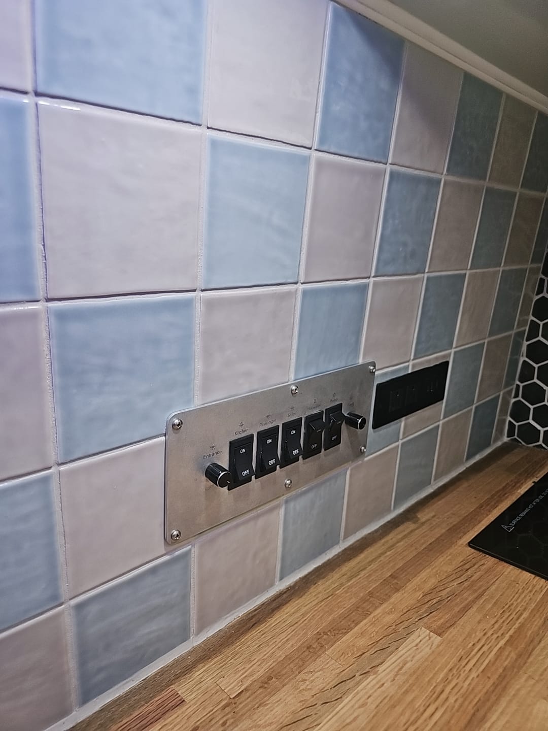 RV rental interior: control panel for Kitchen, Passenger, Sink, Hot water, Pump. Tiled backsplash, wood counter. Ideal for visually impaired.