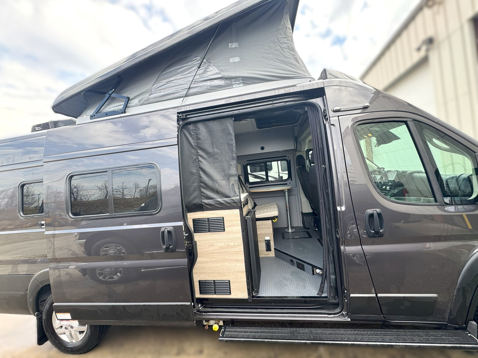 Pop-top rv rental with open side door revealing its compact living area, complete with a table and seating.