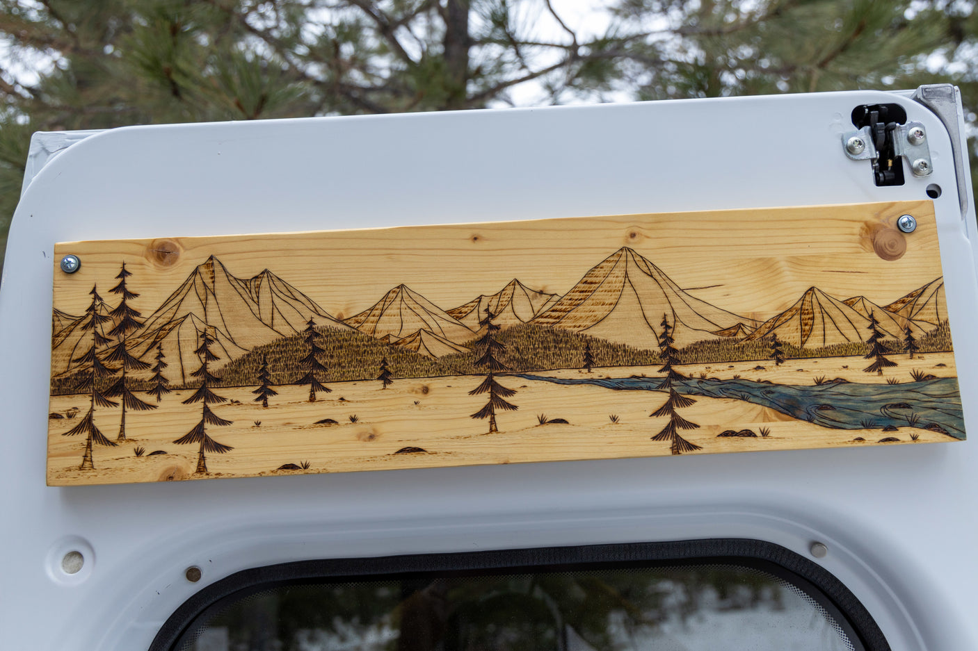 Woodburned mountain & forest art decorates an RV rental interior, showcasing trees and a blue river.